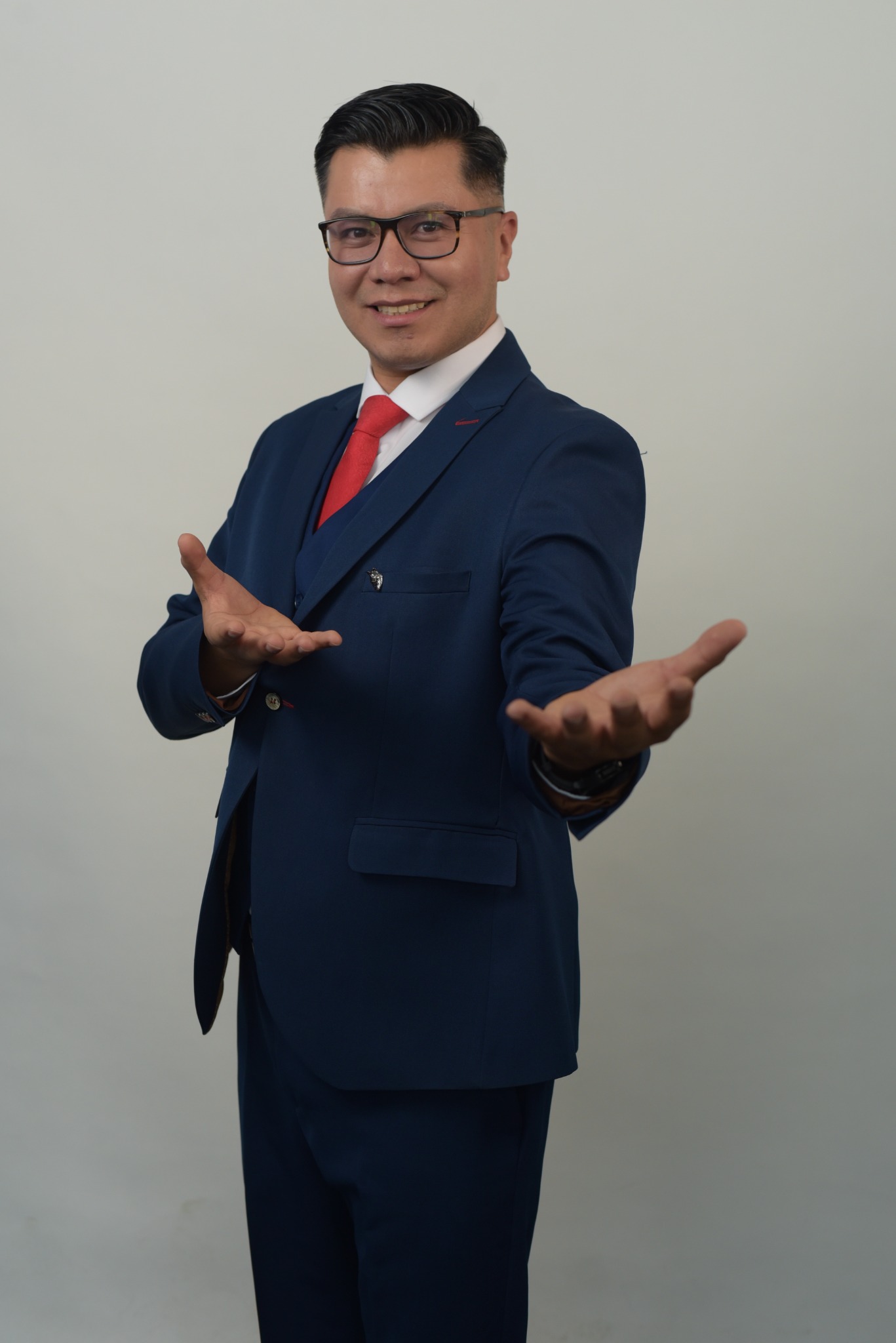 Retrato profesional de Alain Hernández de pie con traje azul y las manos abiertas